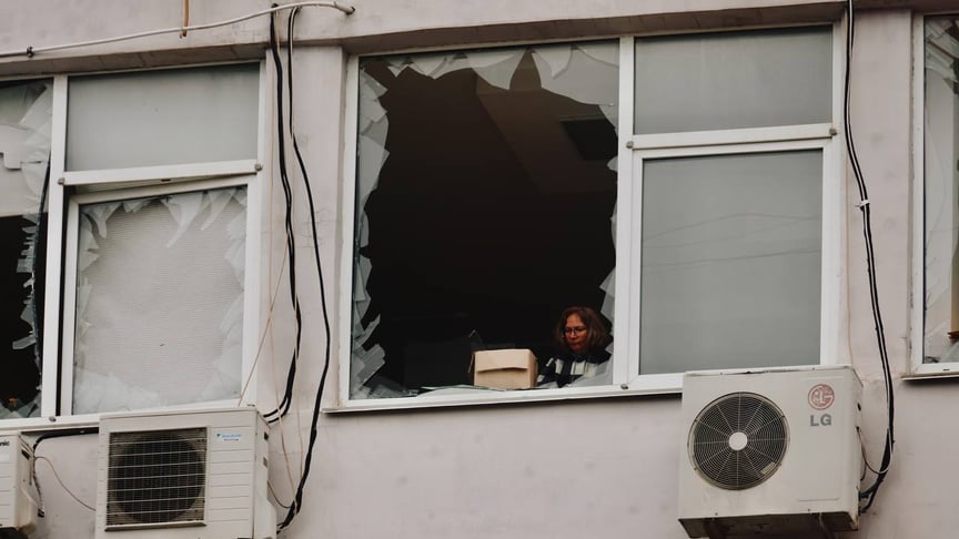 Женщина выглядывает из поврежденного окна дома в Одессе после российской атаки, 12 февраля 2026 года