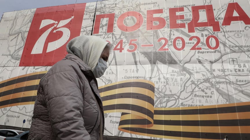An elderly woman wearing a protective face mask walks in front of a giant poster reading 'The Victory 1945-2020' in Moscow, Russia, 27 March 2020.
