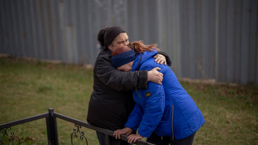 Женщины обнимаются, оплакивая смерть своих мужей во время эксгумации четырех мирных жителей, убитых и похороненных в братской могиле в Микуличах Киевской области, 17 апреля 2022 года