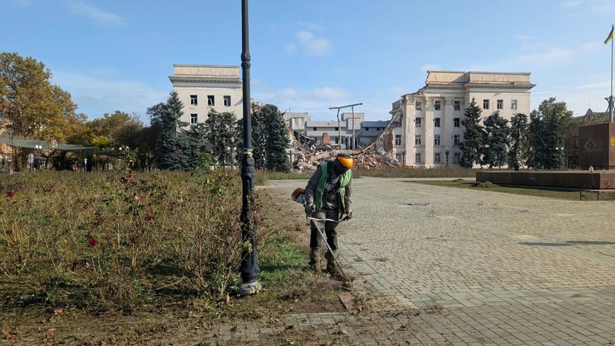 оловік косить траву на фоні зруйнованої будівлі в Херсоні Чоловік косить траву на фоні зруйнованої будівлі в Херсоні