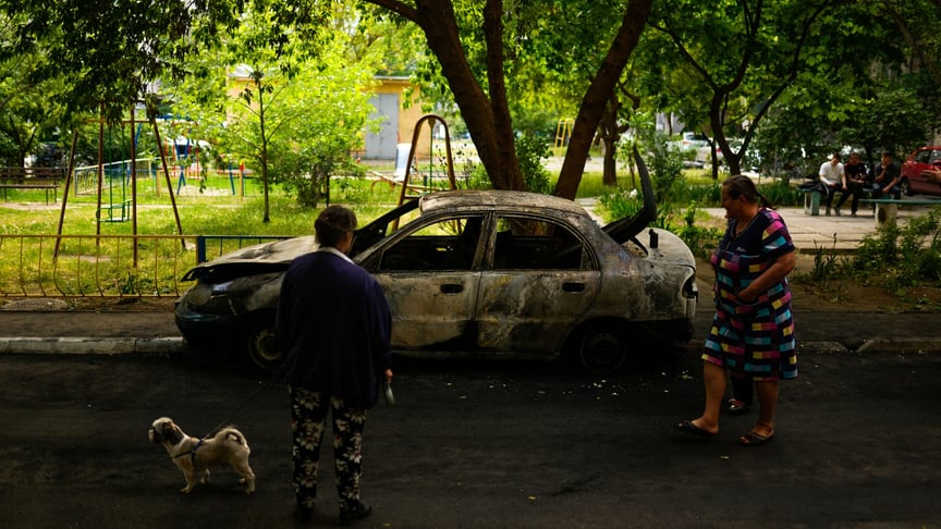 Местные жители смотрят на сгоревший при взрыве автомобиль в Николаеве, 16 мая 2022 года