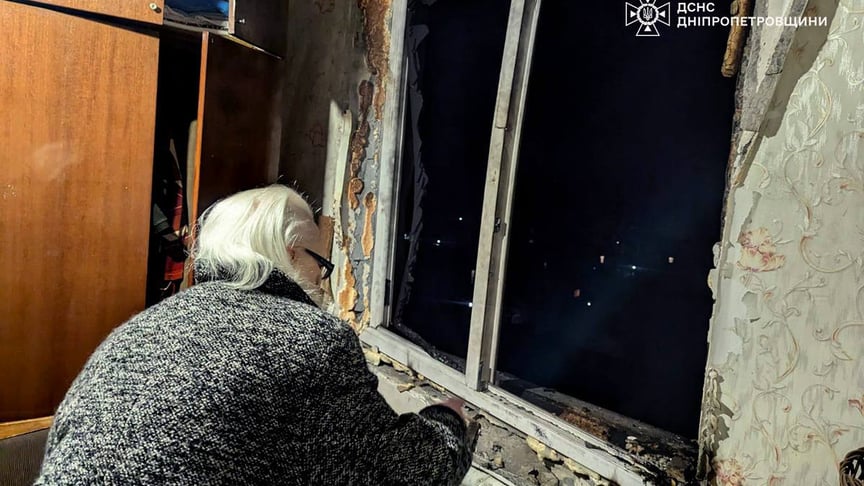 Жінка дивиться на вибите вікно після російської атаки