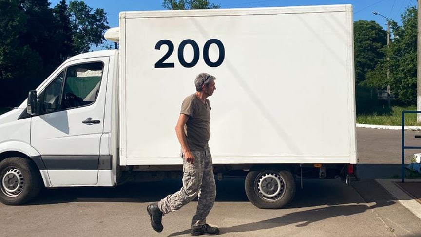 Oleh, the volunteer who delivers the bodies of the dead, next to his vehicle