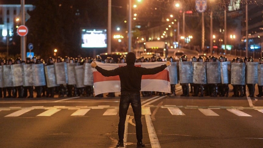 Демонстрант держит флаг перед полицией во время акции протеста после закрытия избирательных участков на президентских выборах в Минске, Беларусь, 9 августа 2020 года.