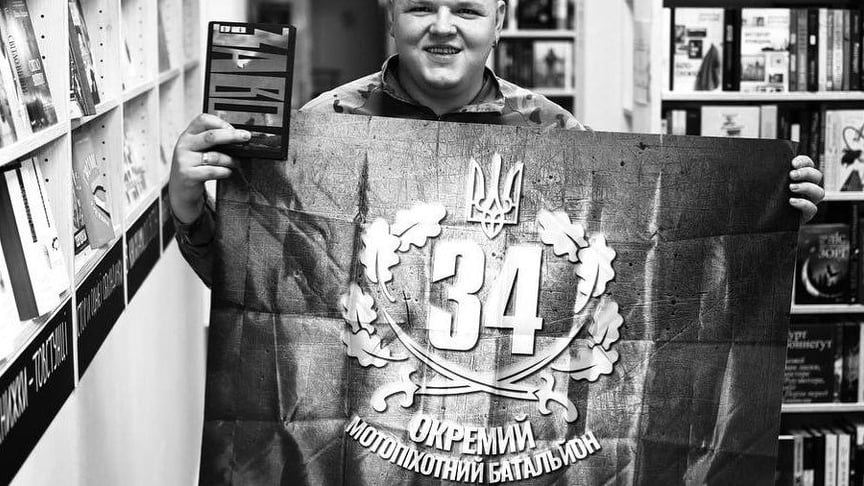 Ігор Мисяк позує зі своїм романом «Завод» і прапором 34-го окремого моторизованого батальйону